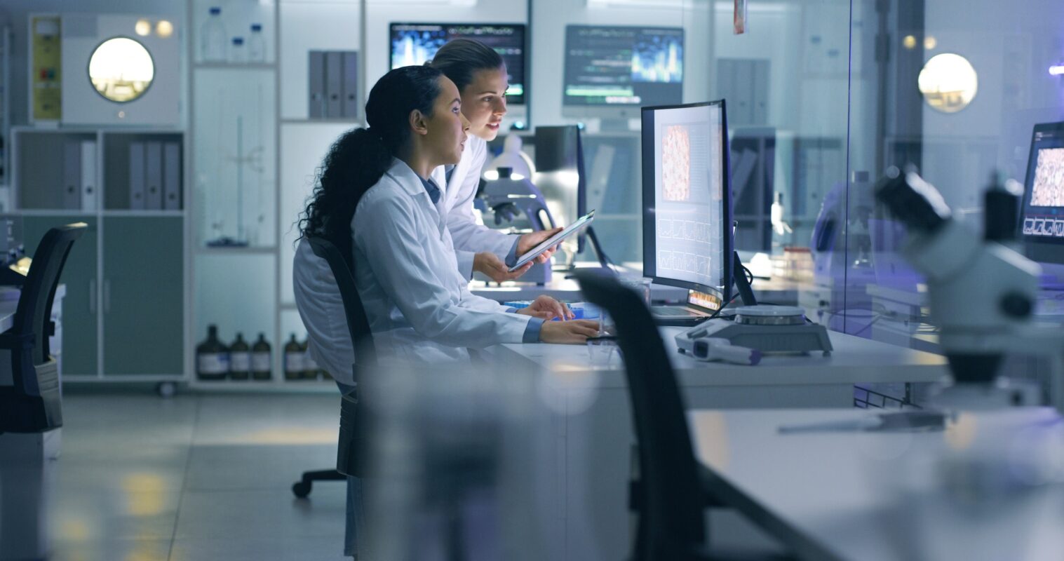 Focused, serious medical scientists analyzing research scans on a computer, working late in the laboratory. Lab workers examine and talk about results from a checkup while working overtime